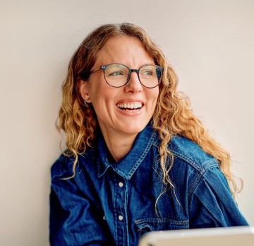 Smiling woman with glasses in denim button-down.